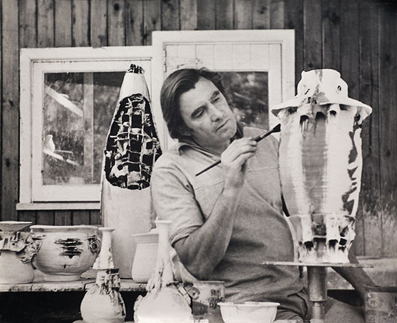 Gus McLaren potter, painting glazes on his large stoneware pottery, with exhibition pieces around him in his studio in Warrandyte, Australia